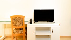 A room with a white desk, a television, and a floral-patterned chair.