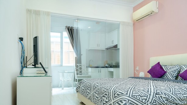 A bedroom with a bed, a desk, and a kitchenette.