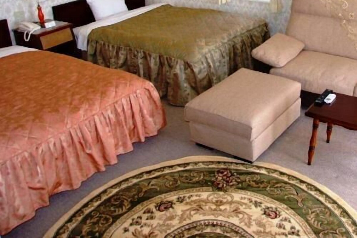 A hotel room with two beds, a sofa, an ottoman, a small table, and a patterned rug.