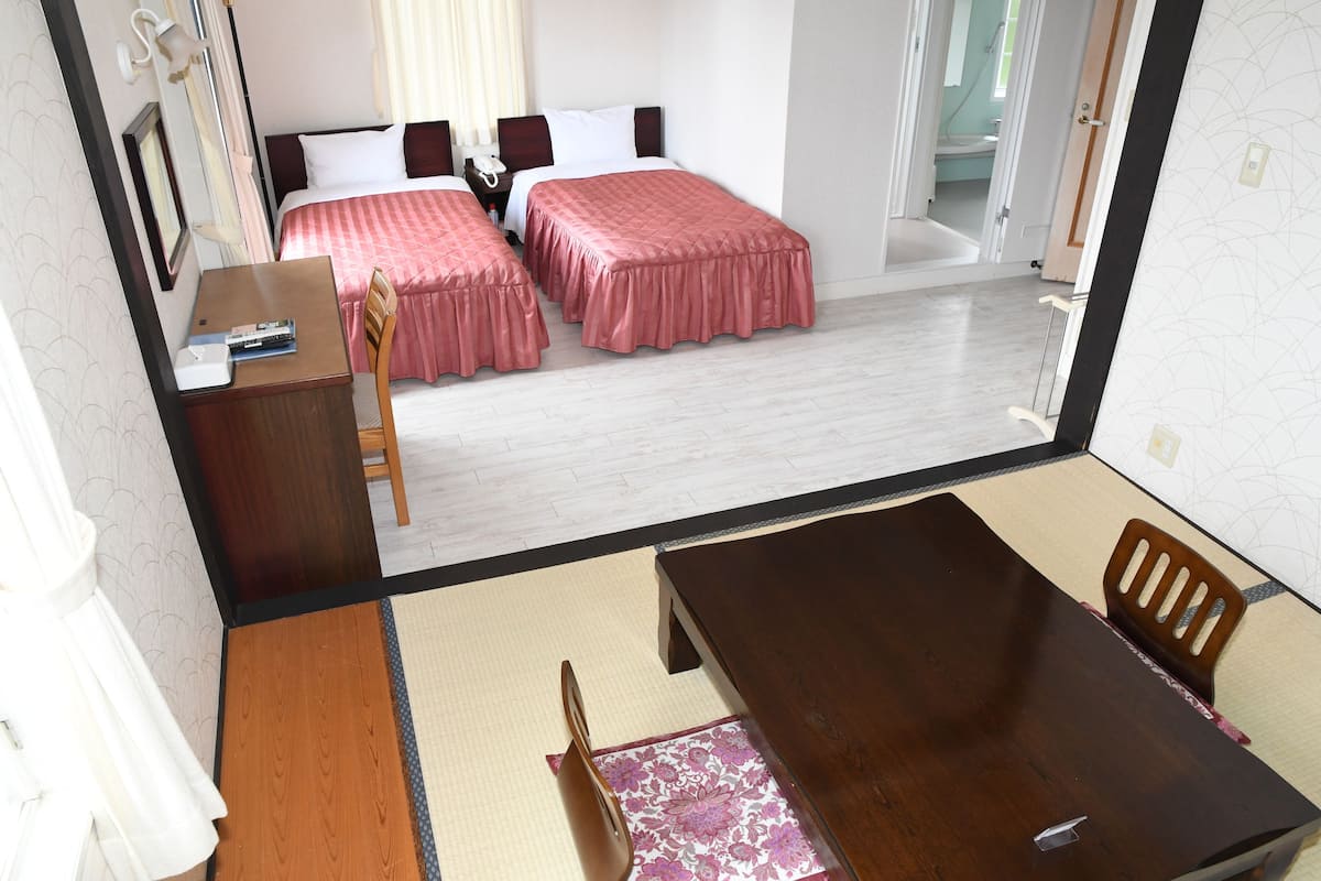 A hotel room with two beds, a wooden desk, a dining table, and a chair.