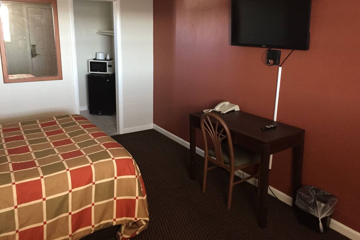 A hotel room with a bed, a desk with a telephone, a television, and a microwave in the corner.
