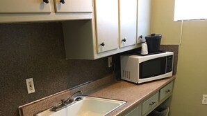 A compact kitchen with a sink, a microwave, and a dishwasher. - Red Carpet Motel (Edmond)