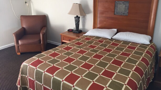 Ein Hotelzimmer mit einem großen Bett, einem hölzernen Kopfteil, einem braunen Ledersessel, einem Nachttisch mit Lampe und einer Klimaanlage an der Wand.