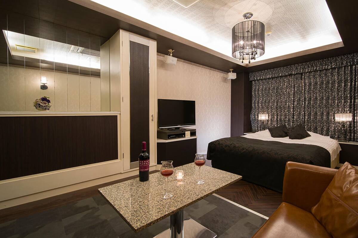 A modern hotel room with a large bed, a seating area with a table, a minibar, and a television.