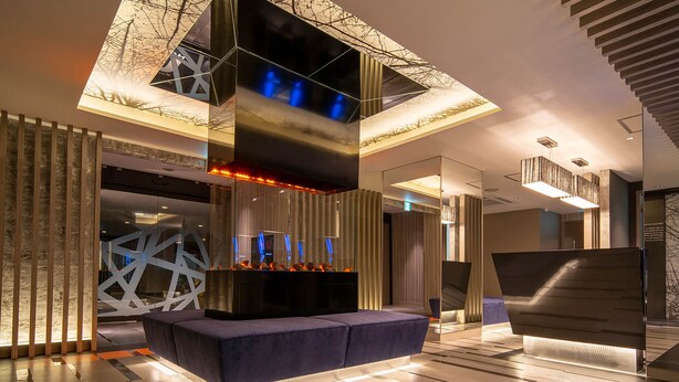 A modern lobby with a central seating area, a large digital display, and a geometric decorative wall. - HOTEL U's Kouroen – Adults Only (Nishinomiya)