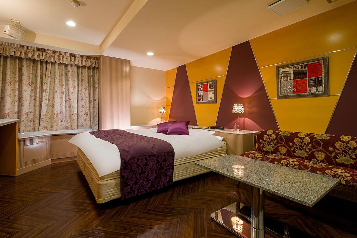 A hotel room with a bed, a sofa, a small table, and a window with curtains.
