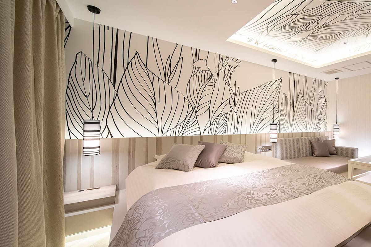 A modern hotel room with a large bed, a seating area, and a decorative ceiling.
