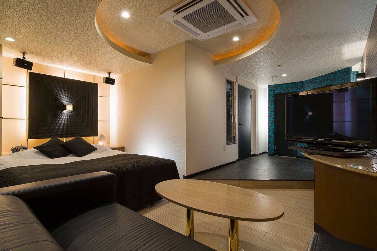 A modern hotel room with a bed, sofa, TV, and a small table.