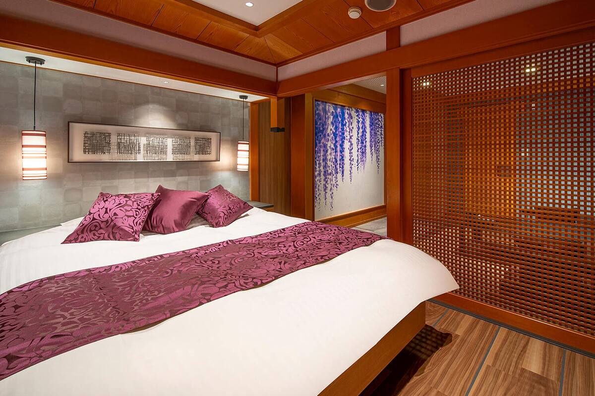 A modern bedroom with a large bed, a wooden headboard, a decorative wall, and a sliding wooden screen.