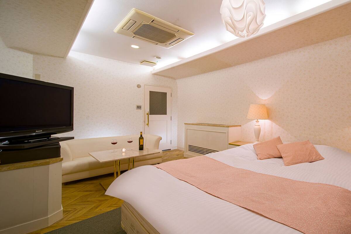A hotel room with a bed, a television, a desk, and two lamps.
