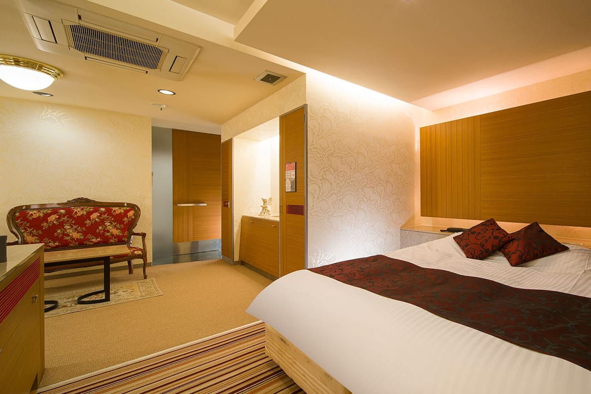 A hotel room with a large bed, a wooden headboard, a bench, and a desk.