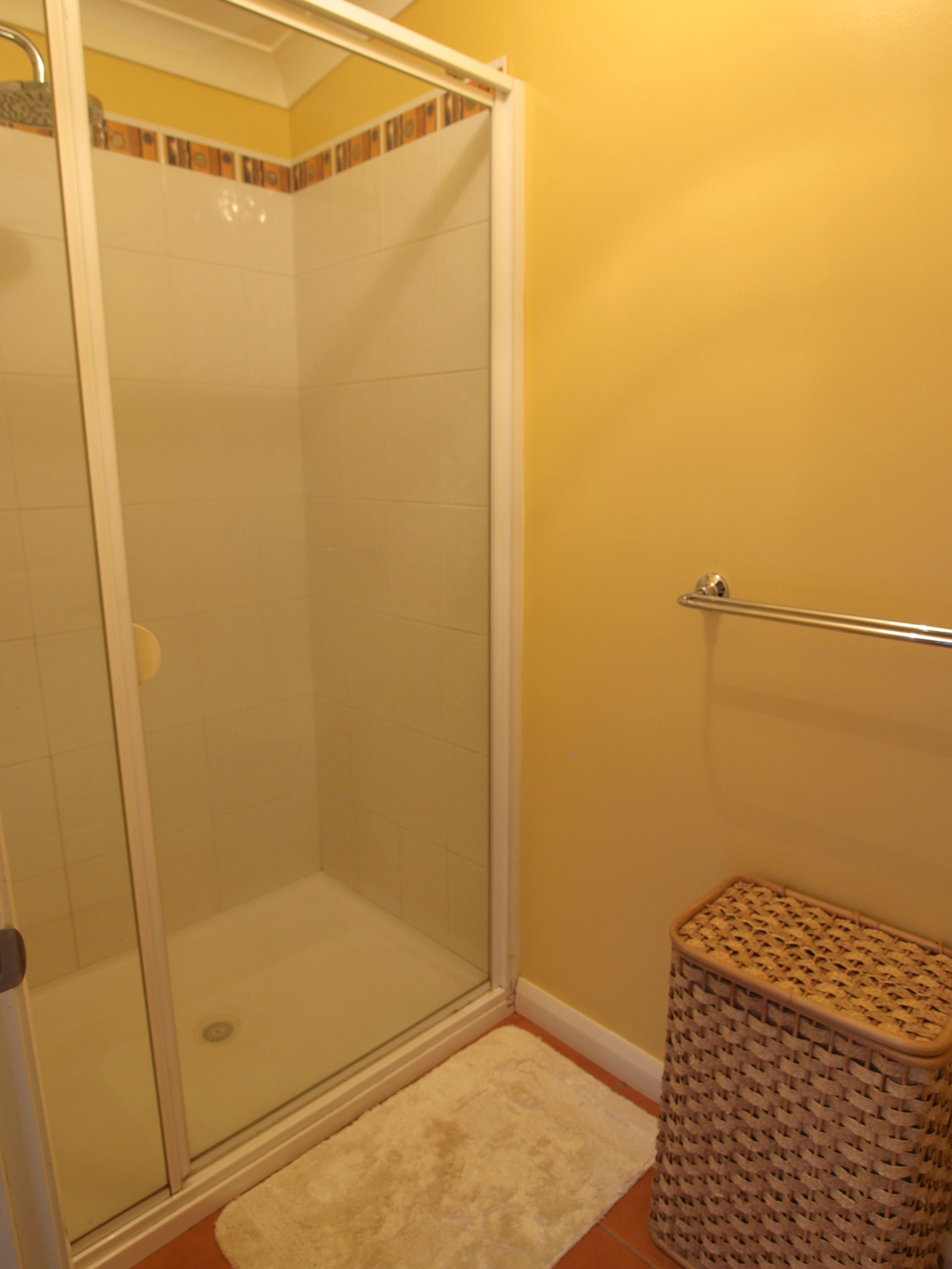 A shower area with a glass door, a white rug, and a wicker basket.