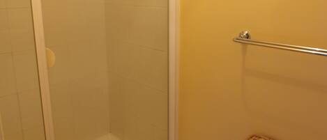 A shower area with a glass door, a white rug, and a wicker basket.