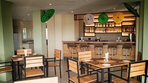 Un restaurant avec des tables et des chaises en bois, un coin bar avec des bouteilles exposées et des parasols décoratifs.