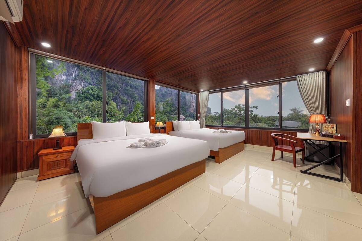 A spacious bedroom with two large beds, wooden headboards, and a large window offering a view of a mountainous landscape.