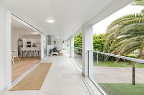 A modern, open-plan living area with a kitchen, dining space, and a balcony with a view of greenery. - Pura Vida (Noosaville)