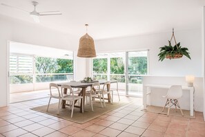 A bright dining area with a round table, white chairs, and a hanging plant.