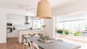 Une cuisine moderne avec des meubles blancs, un coin repas comprenant une table et des chaises, et une grande fenêtre donnant sur un paysage verdoyant.