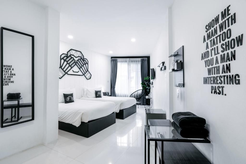 A modern hotel room with a large bed, a desk, and a mirror. There is a wall with a motivational quote and a framed picture.