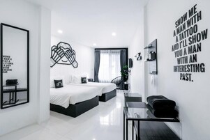A modern hotel room with a large bed, a desk, and a mirror. There is a wall with a motivational quote and a framed picture.