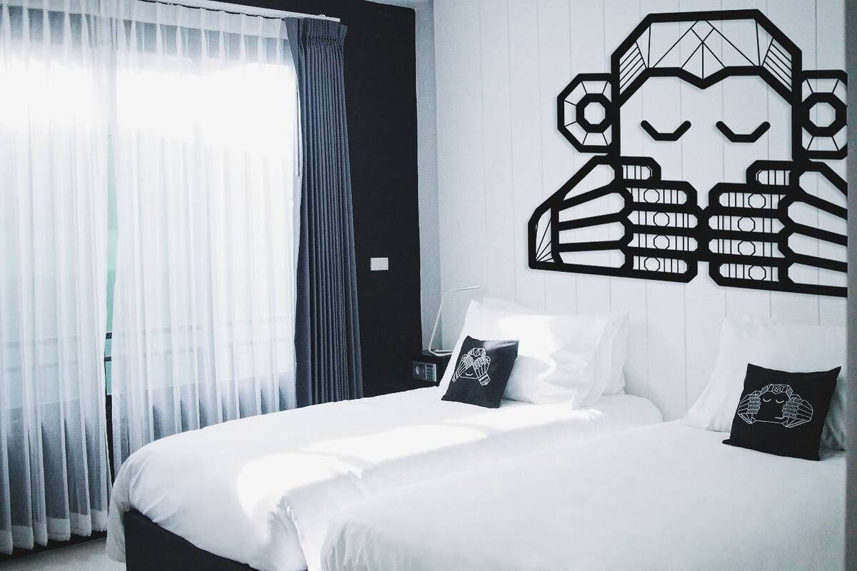 Une chambre d’hôtel avec un lit, du linge de lit blanc, un élément de décoration murale et une fenêtre avec des rideaux.
