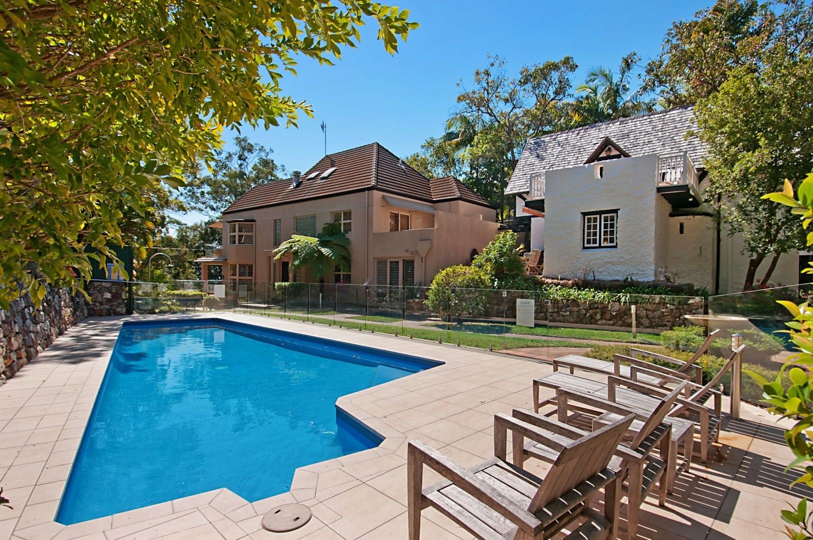A rectangular swimming pool with a tiled deck, surrounded by a stone wall and wooden deck chairs.