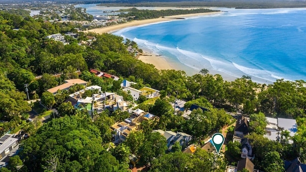 Vista aérea de uma área costeira com praia, edifícios residenciais e uma montanha ao fundo.