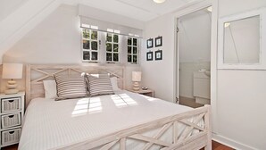Quarto com cama, mesas de cabeceira, janela e porta.