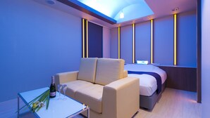 A modern hotel room with a sofa, a small table with a bottle and glasses, and a bed with a headboard. - HOTEL IRIS - Adult Only (Fujisawa)