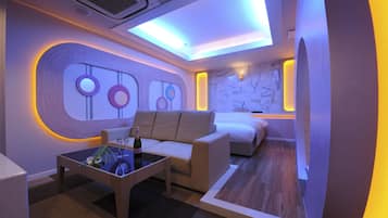 A modern hotel room with a sofa, a small table with a bottle and glasses, and a bed.