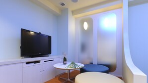 A modern room with a flat-screen TV, a small round table with a bottle and glasses, a cushioned bench, and a curved wall feature. - HOTEL IRIS - Adult Only (Fujisawa)