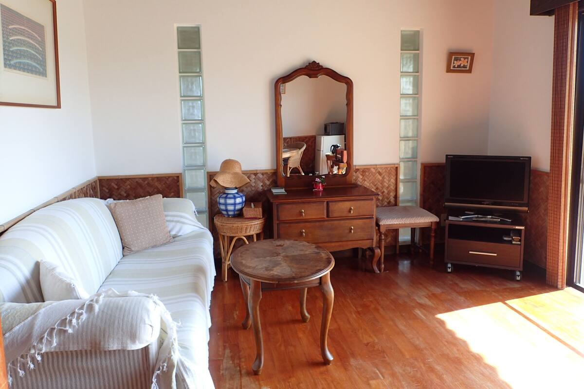 A living room with a sofa, a wooden coffee table, a dresser, a television, and a mirror.
