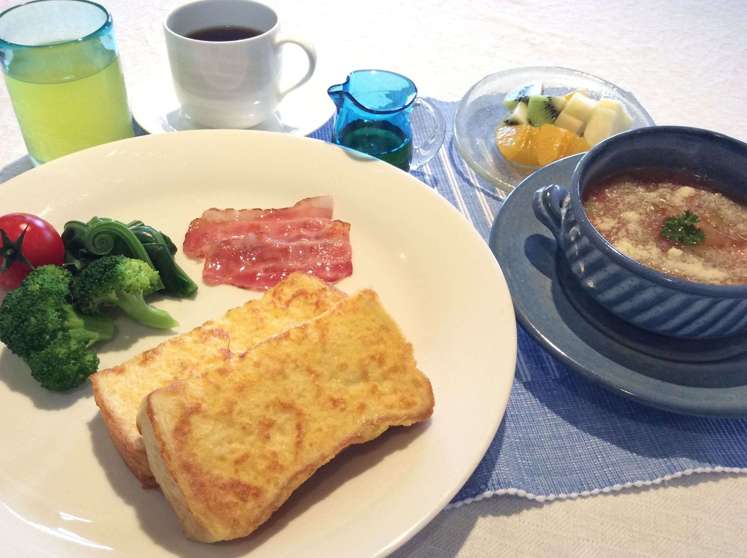 A plate with toast, bacon, tomatoes, broccoli, and a bowl of soup.