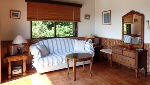 A cozy room with a sofa, a small round table, a dresser, and a large mirror. - MaYaGuSuKu RESORT (Taketomi)