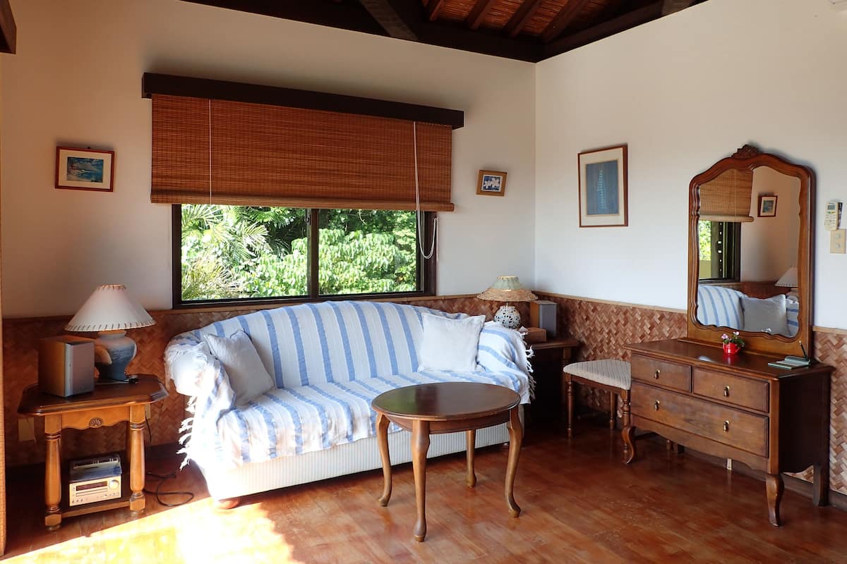 A cozy room with a sofa, a small round table, a dresser, and a large mirror.