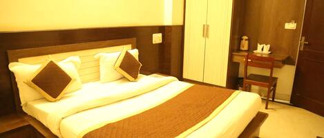 A neatly made bed with a brown bedspread and white linens, a wooden headboard, and a wooden wardrobe with a mirror and a small table beside it.