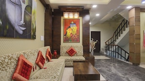 A lobby with a sofa, a coffee table, a staircase, and a large painting on the wall. - Hotel Sagun (Jaipur)