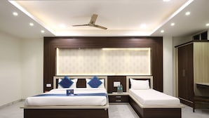 A modern hotel room with two beds, a ceiling fan, recessed lighting, and a large window with blinds. - Hotel Sagun (Jaipur)