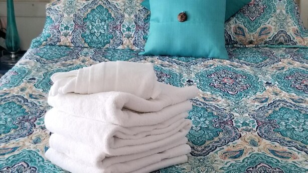 A bed with a patterned bedspread, a teal pillow, and a stack of white towels. - Popular   ~ Quaint. Bogue Shores Condo --  just steps to a beautiful beach (Atlantic Beach)