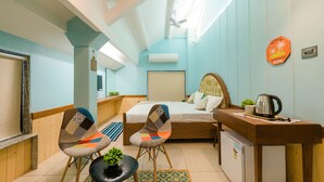 Habitació d'hotel senzilla amb llit, dues cadires, escriptori, nevera petita i ventilador de sostre.