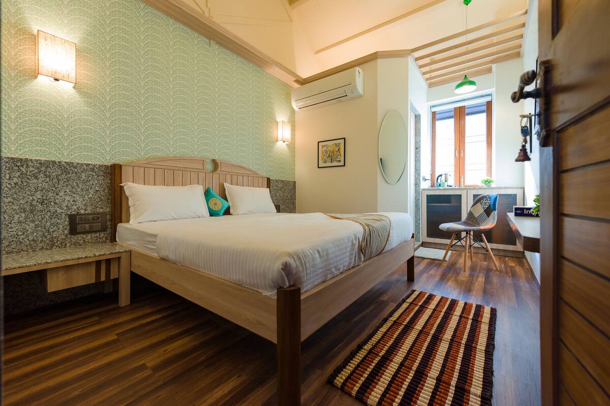 Une chambre avec un lit en bois, un banc, un mur à motifs, un climatiseur, un bureau et une chaise.