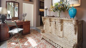 A room with a wooden desk, a chair, a patterned floor, a decorative cabinet, a mirror, and a vase with flowers. - Hotel Boutique La Indiana de Begur - Adults Only (Begur)