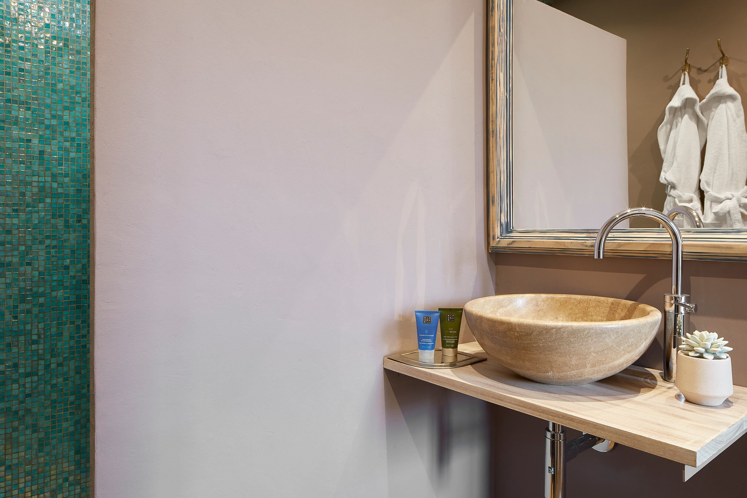 A bathroom with a beige stone sink, a mirror, and a small potted succulent.