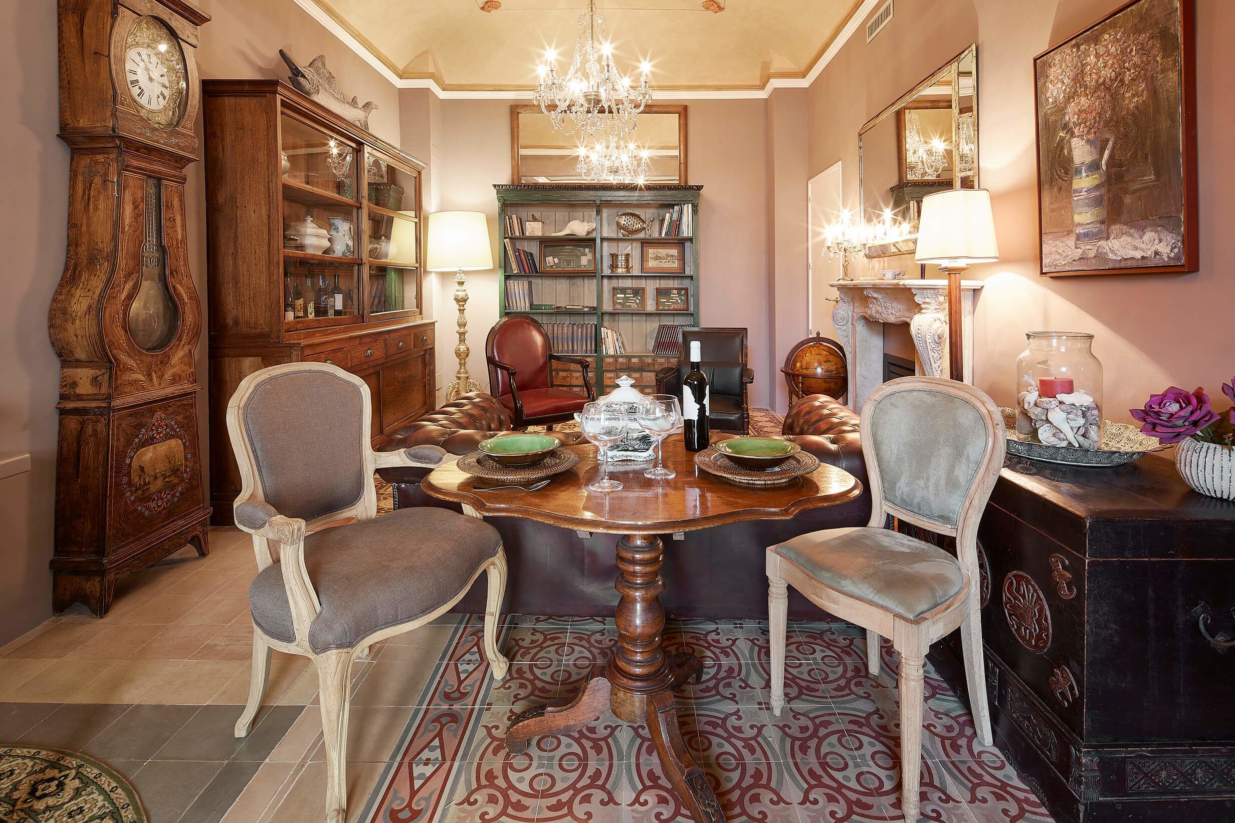 Een eetkamer met een houten tafel, stoelen, een kroonluchter en een boekenkast.