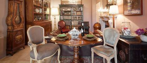 Een eetkamer met een houten tafel, stoelen, een kroonluchter en een boekenkast.