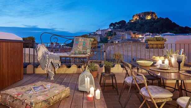 A rooftop terrace with a wooden deck, outdoor furniture, candles, and a view of a hilltop town. - Hotel Boutique La Indiana de Begur - Adults Only (Begur)