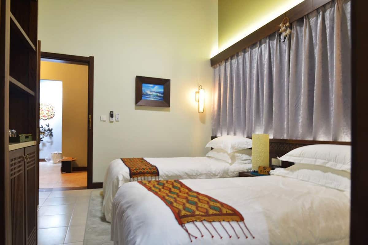 A hotel room with two beds, a nightstand, a wall-mounted lamp, and a picture of a beach.