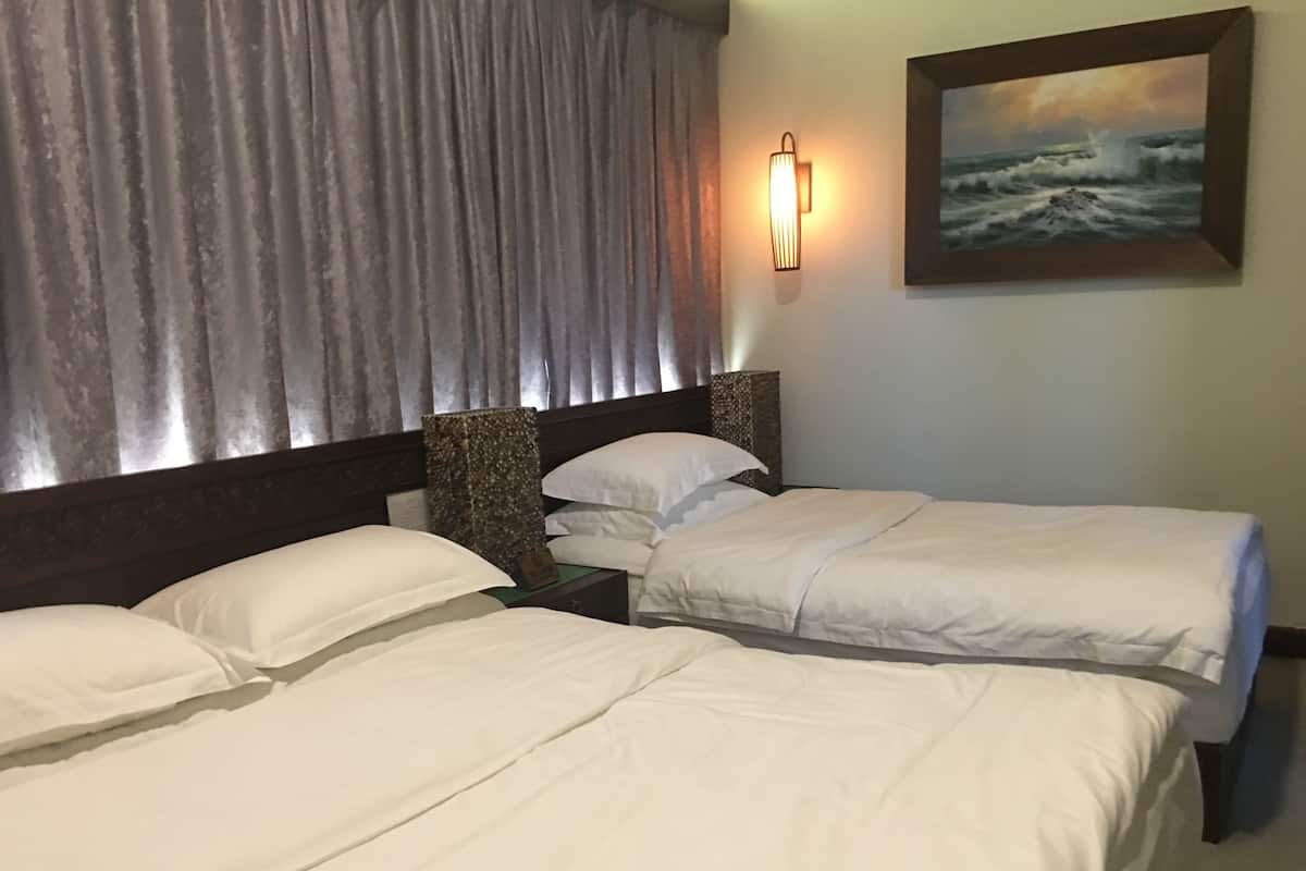 A hotel room with two beds, a nightstand, a lamp, and a painting of a seascape.