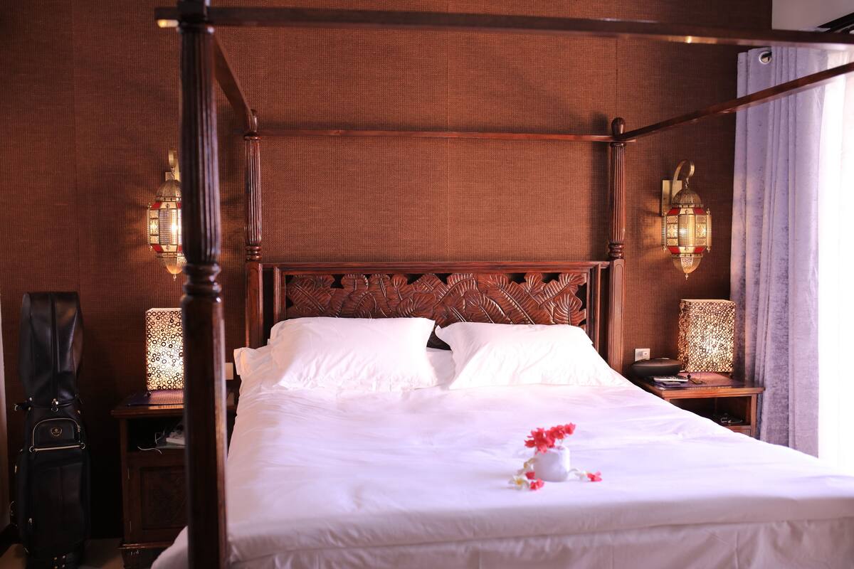 A four-poster bed with white linens, two bedside tables with lamps, and a wooden headboard.