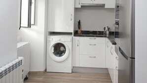 Une cuisine compacte avec des meubles blancs, un lave-linge encastré et un réfrigérateur en acier inoxydable.